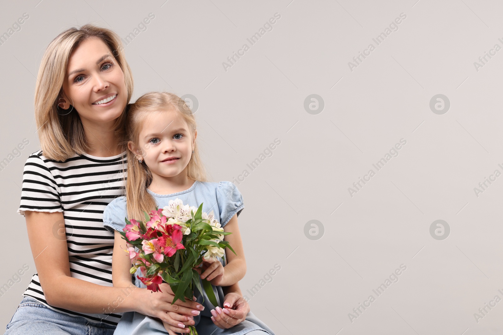 Photo of Happy woman with her daughter and bouquet of alstroemeria flowers on gray background, space for text. Mother's Day celebration