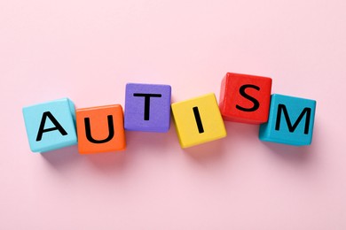 Photo of Word Autism made with colorful cubes on pink background, flat lay