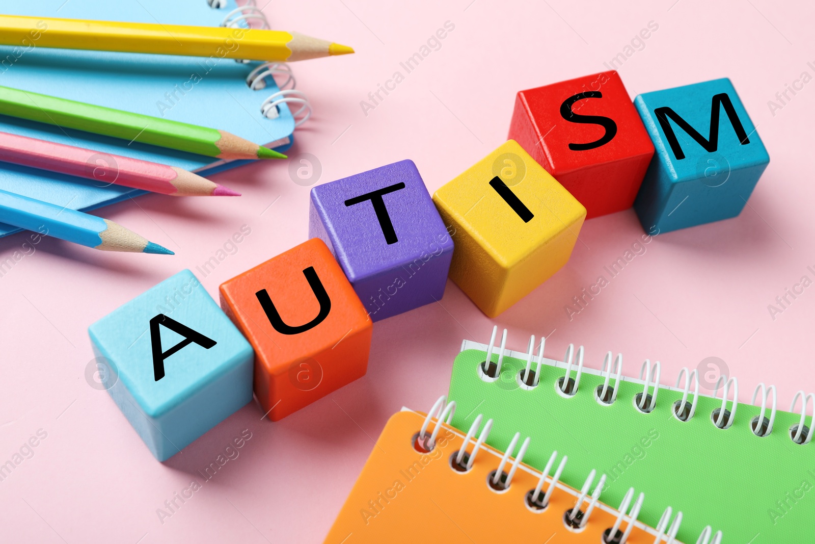 Photo of Word Autism made with colorful cubes, pencils and notebooks on pink background, closeup