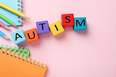 Photo of Word Autism made with colorful cubes, pencils and notebooks on pink background, flat lay