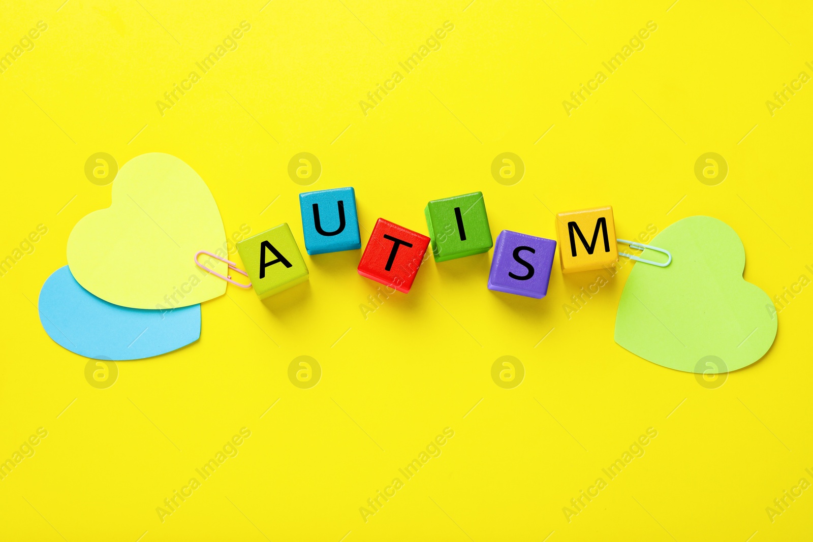 Photo of Word Autism made with colorful cubes and paper hearts on yellow background, flat lay