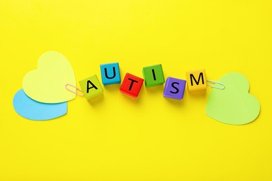 Photo of Word Autism made with colorful cubes and paper hearts on yellow background, flat lay