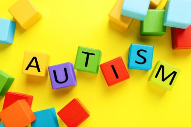 Photo of Word Autism made with colorful cubes on yellow background, flat lay