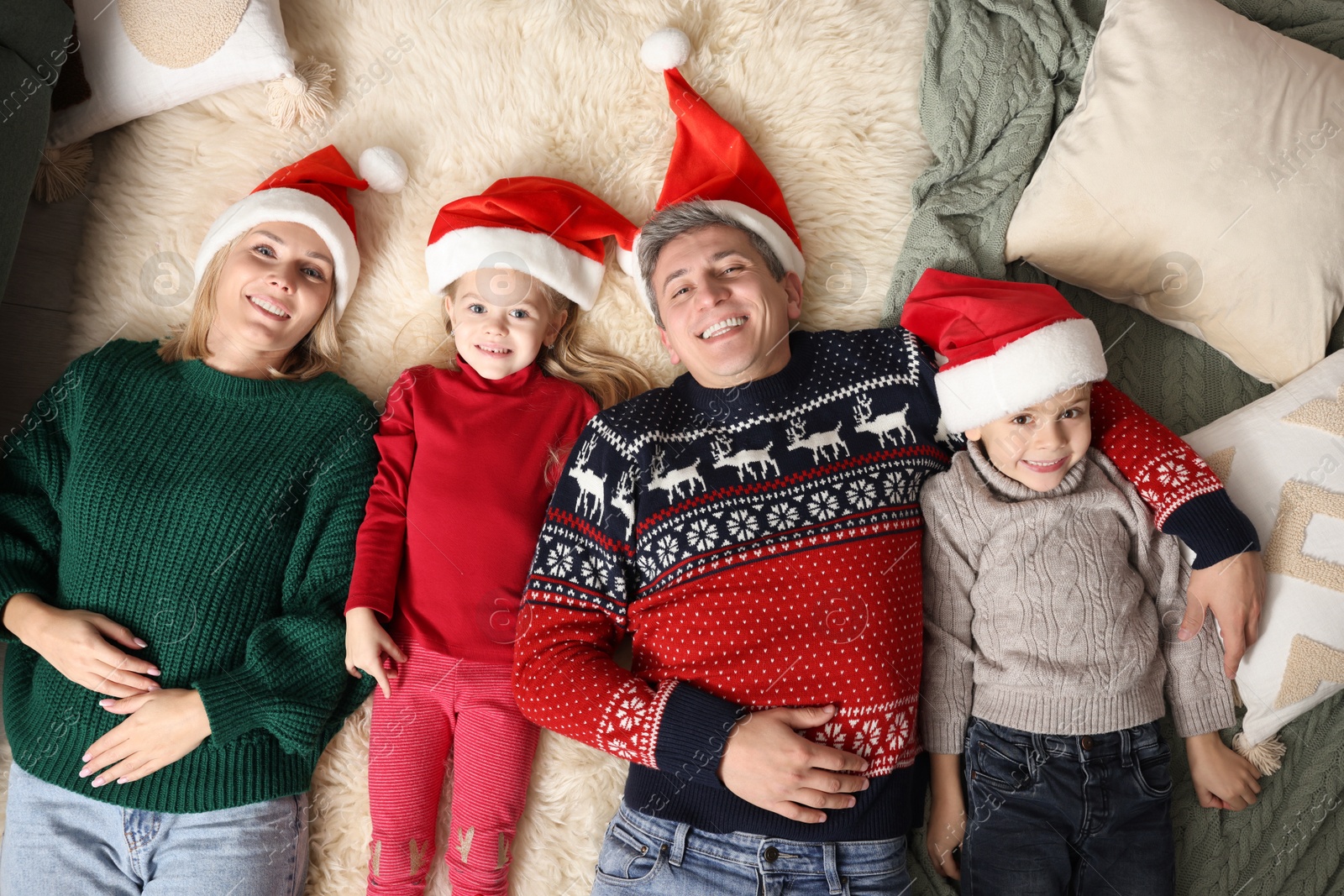 Photo of Happy family in Santa hats lying on rug together, top view. Christmas season