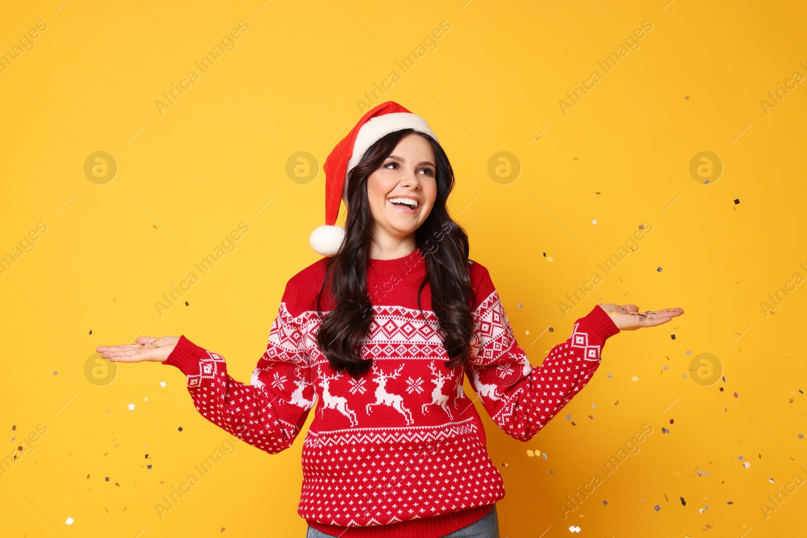 Photo of Beautiful woman in Santa hat and Christmas sweater with confetti on yellow background