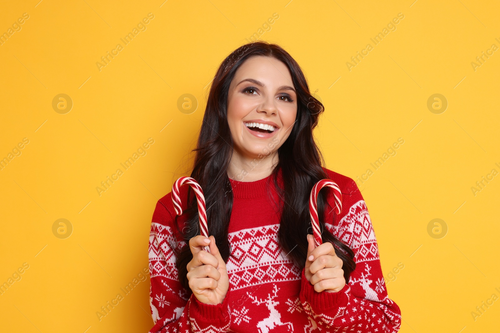 Photo of Excited woman in Christmas sweater with candy canes on yellow background