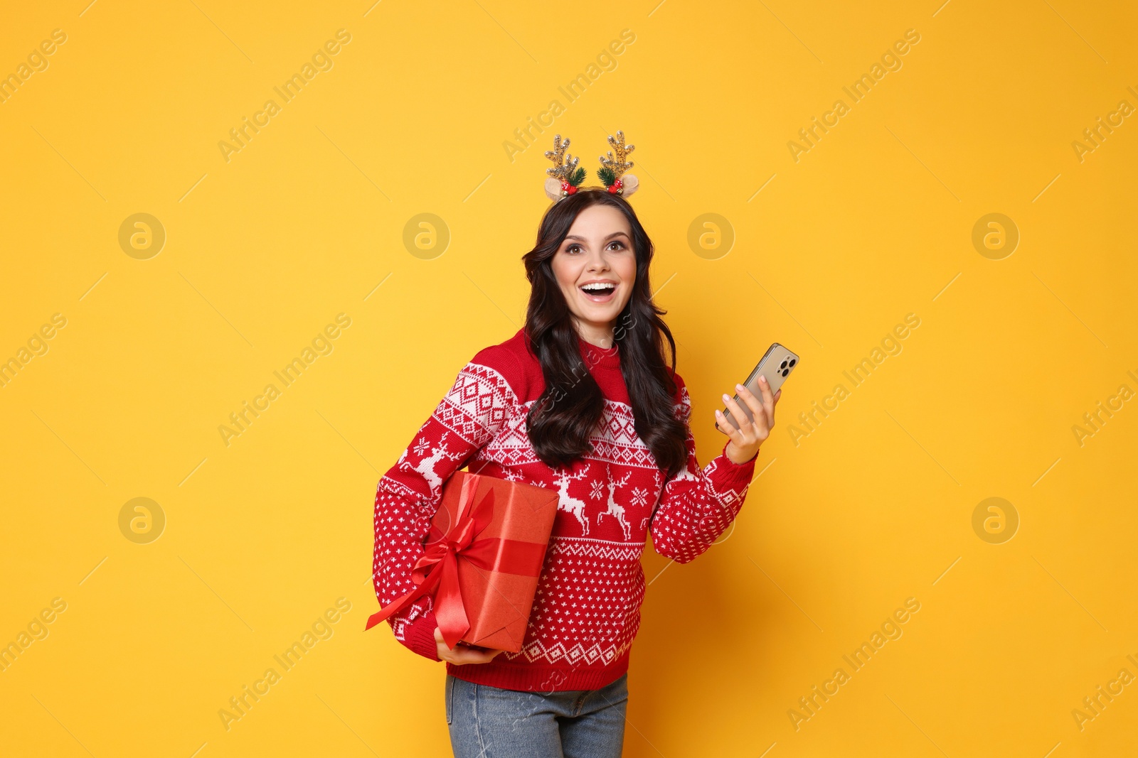 Photo of Happy woman with Christmas gift and smartphone on yellow background