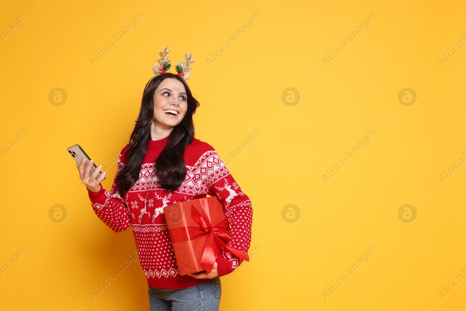 Photo of Happy woman with Christmas gift and smartphone on yellow background, space for text