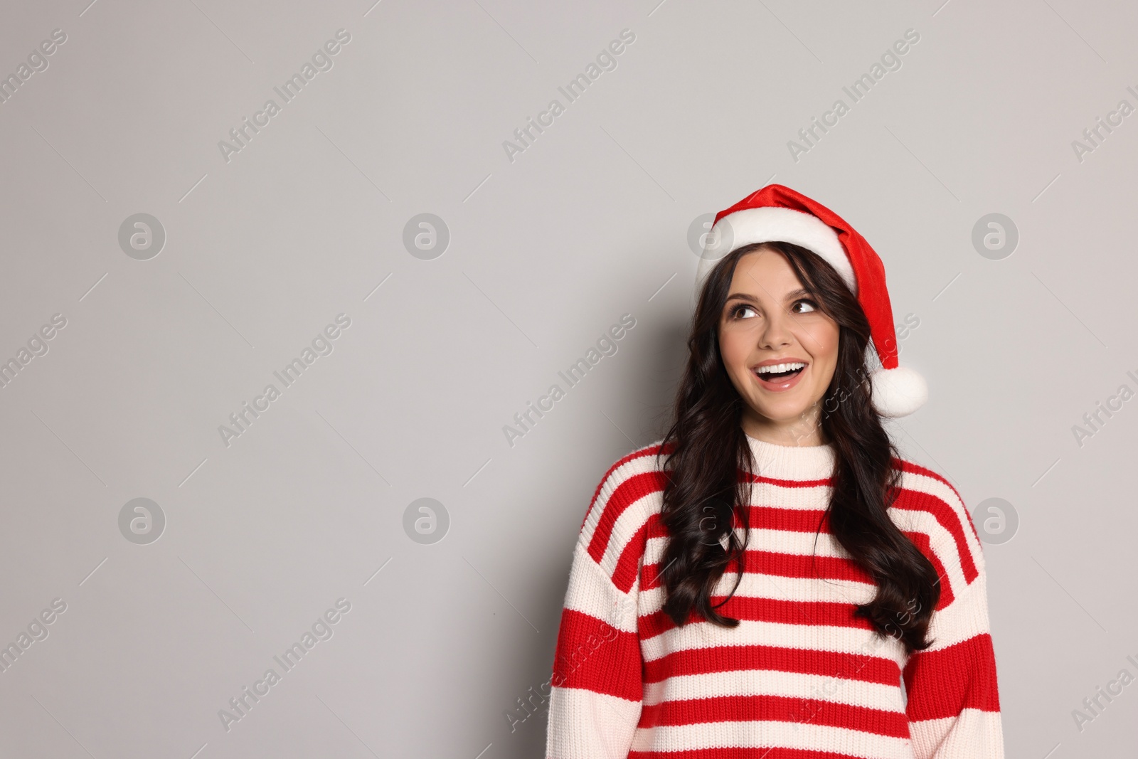 Photo of Beautiful woman in Santa hat on light grey background, space for text. Christmas celebration