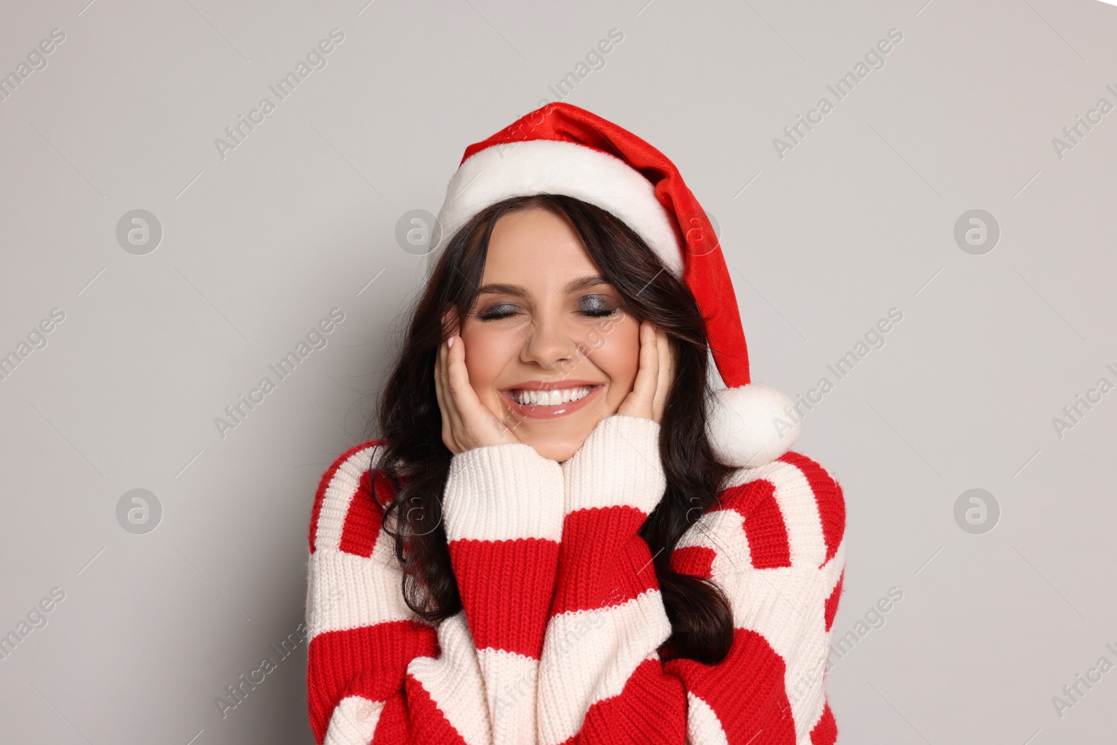 Photo of Beautiful woman in Santa hat on light grey background, space for text. Christmas celebration