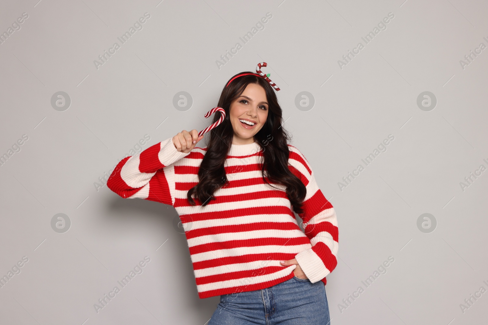 Photo of Happy woman with candy cane on light grey background. Christmas celebration