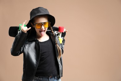 Photo of Little girl with penny board on pale brown background, space for text