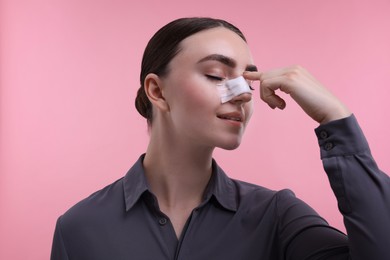 Photo of Woman with medical bandage on her nose after plastic surgery operation against pink background