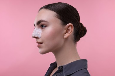 Photo of Woman with medical bandage on her nose after plastic surgery operation against pink background