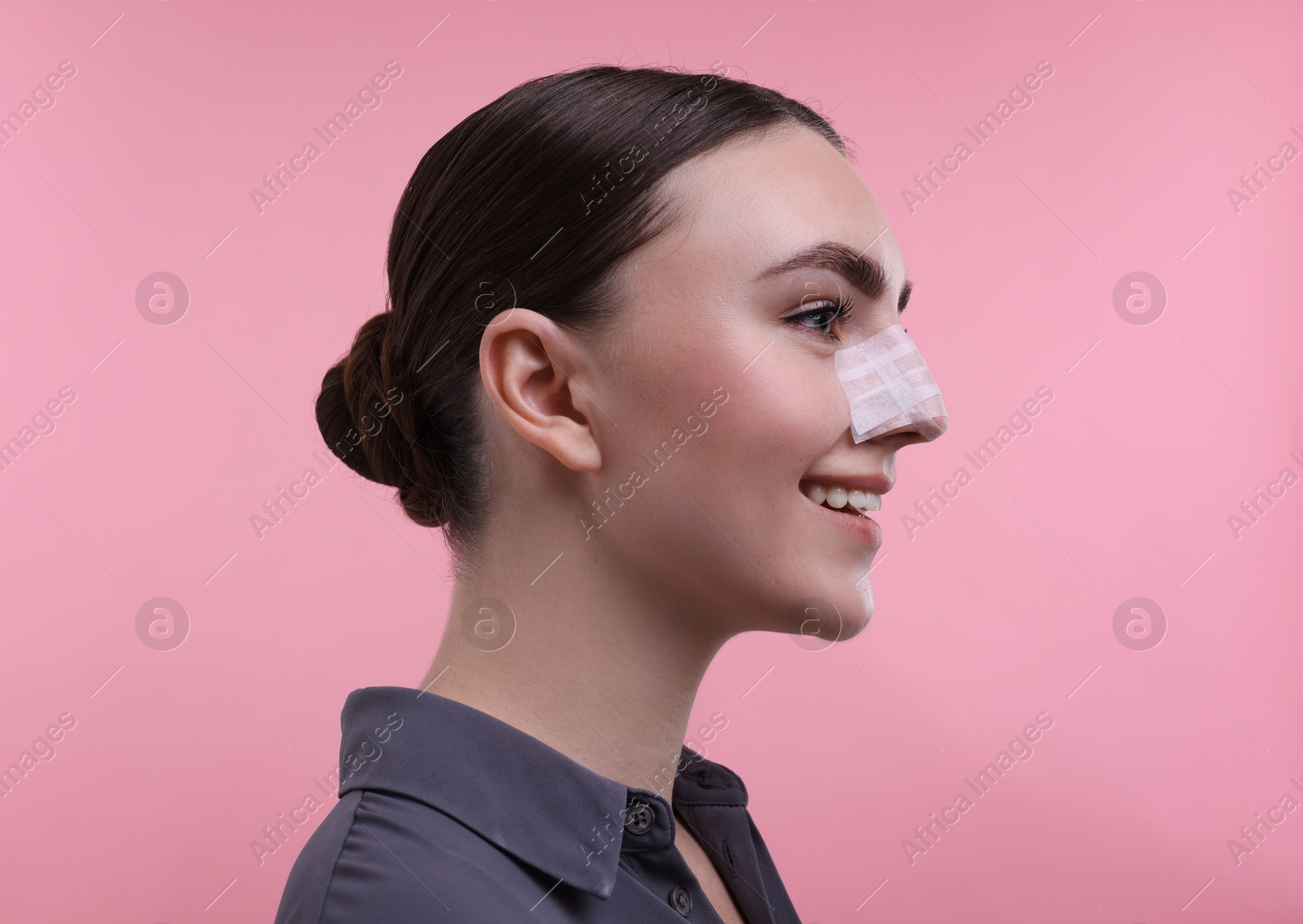 Photo of Woman with medical bandage on her nose after plastic surgery operation against pink background