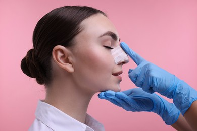 Photo of Doctor checking patient's nose after plastic surgery operation on pink background, closeup