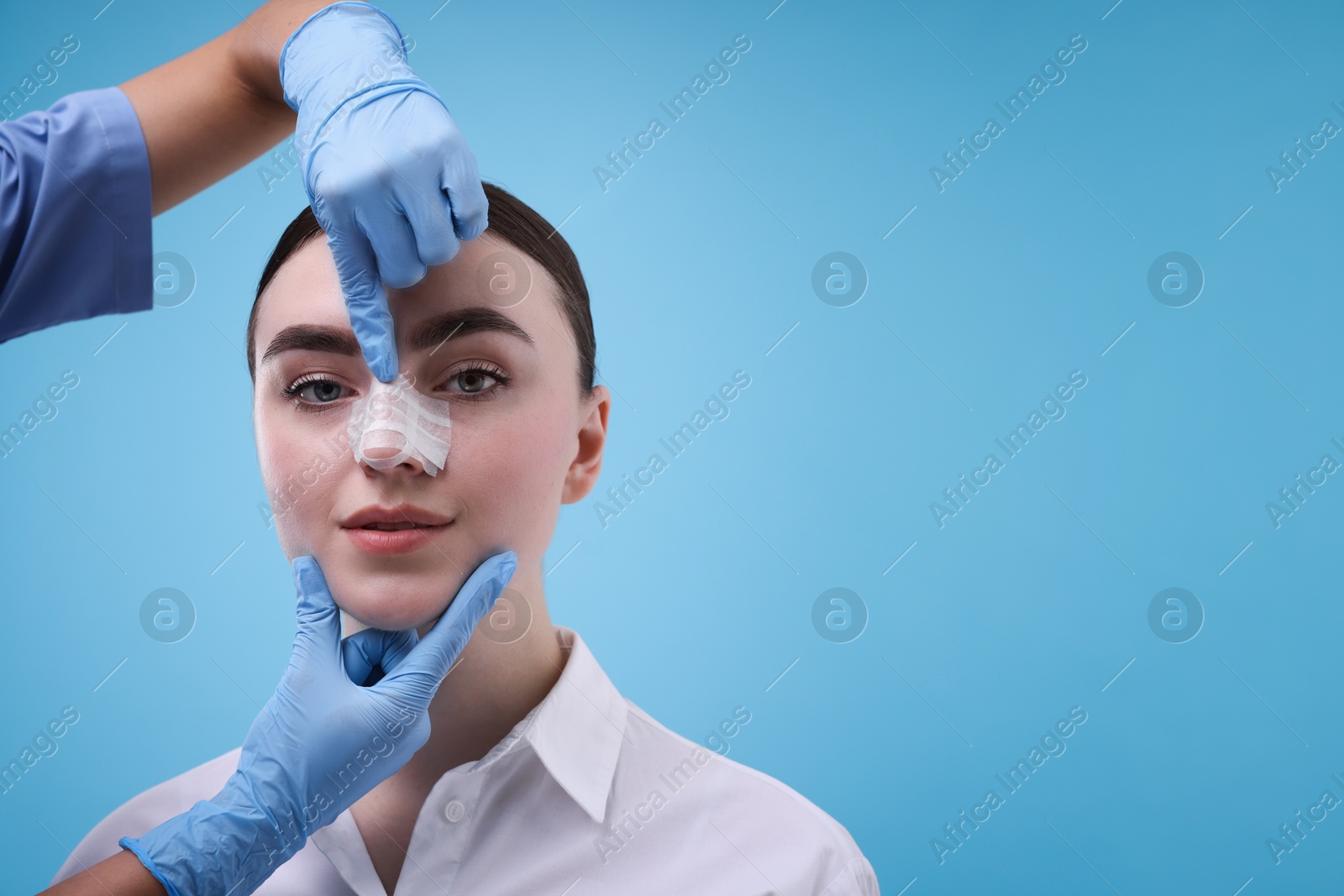 Photo of Doctor checking patient's nose after plastic surgery operation on light blue background, closeup. Space for text