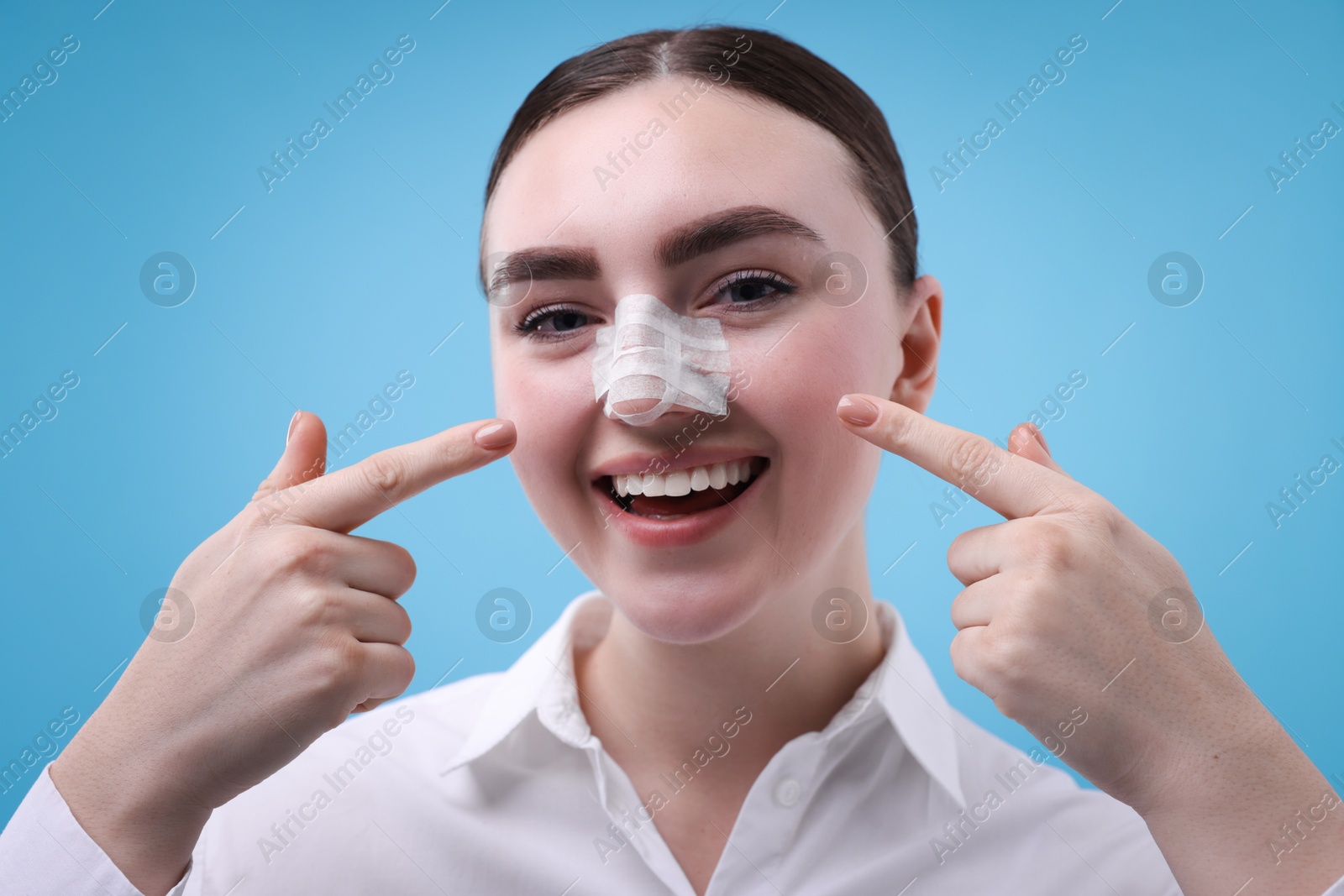 Photo of Woman with medical bandage on her nose after plastic surgery operation against light blue background