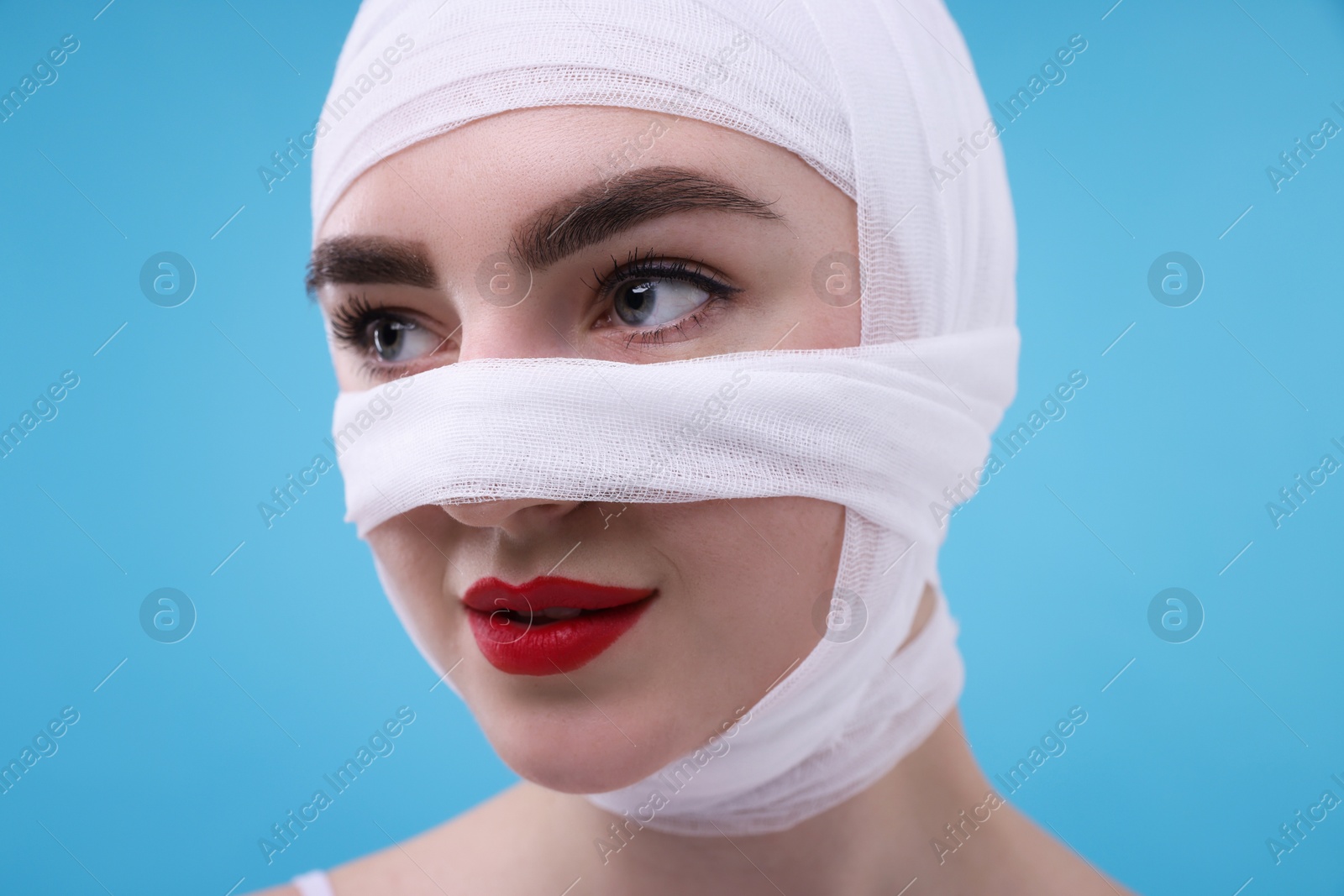 Photo of Woman with nose wrapped in medical bandage after plastic surgery operation on light blue background