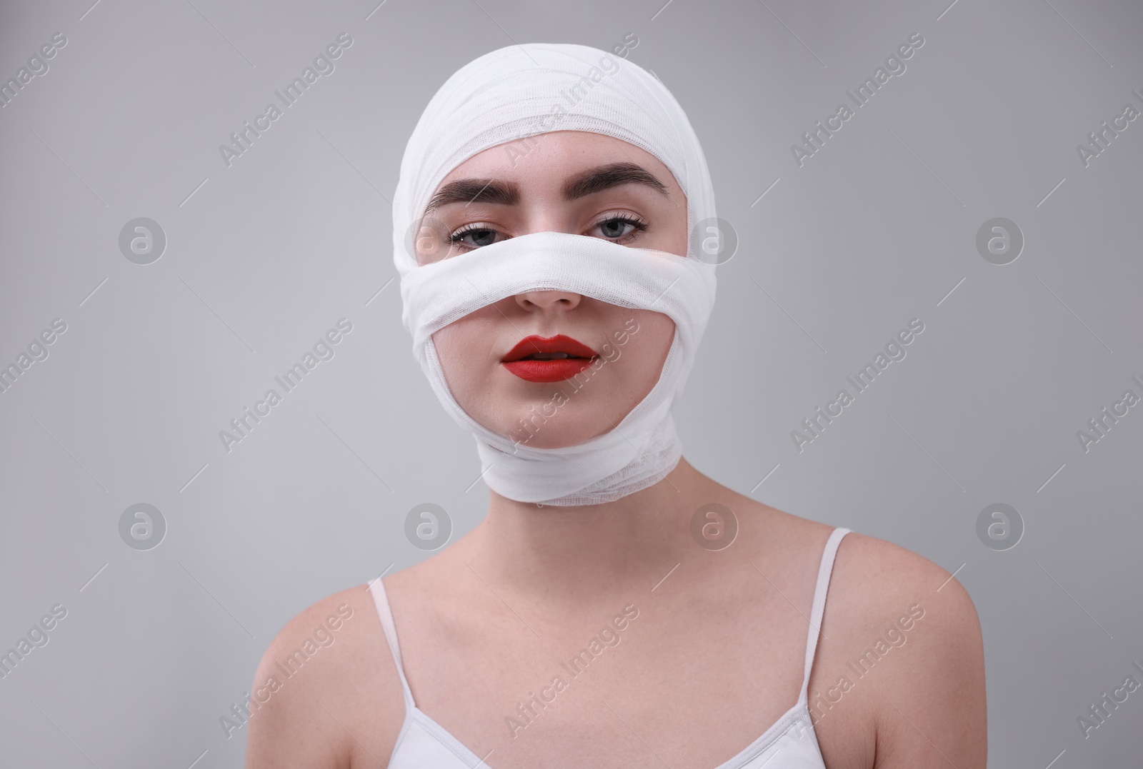 Photo of Woman with nose wrapped in medical bandage after plastic surgery operation on grey background