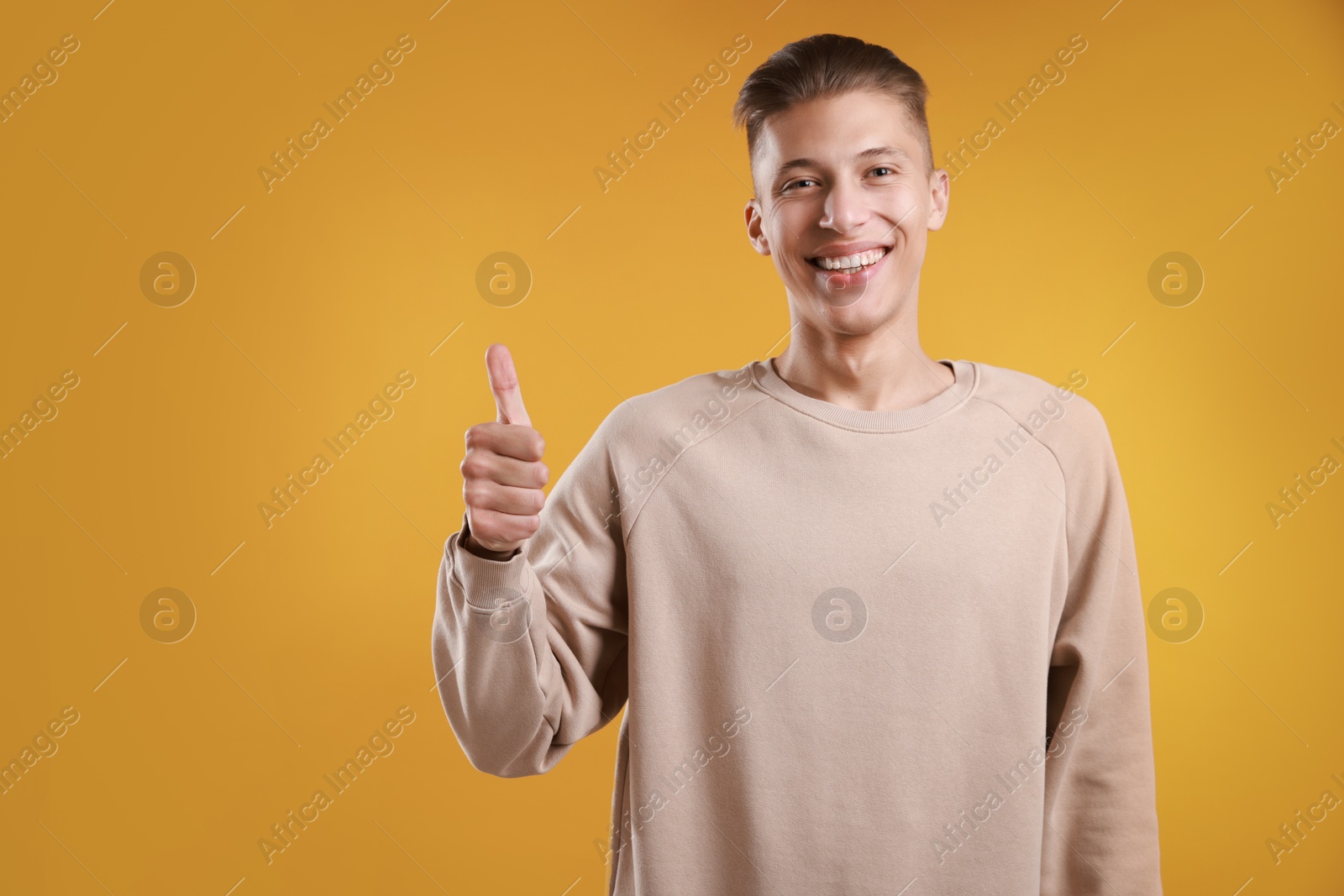 Photo of Happy man showing thumbs up on orange background, space for text. Like gesture