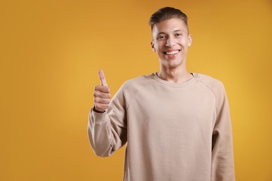 Happy man showing thumbs up on orange background, space for text. Like gesture