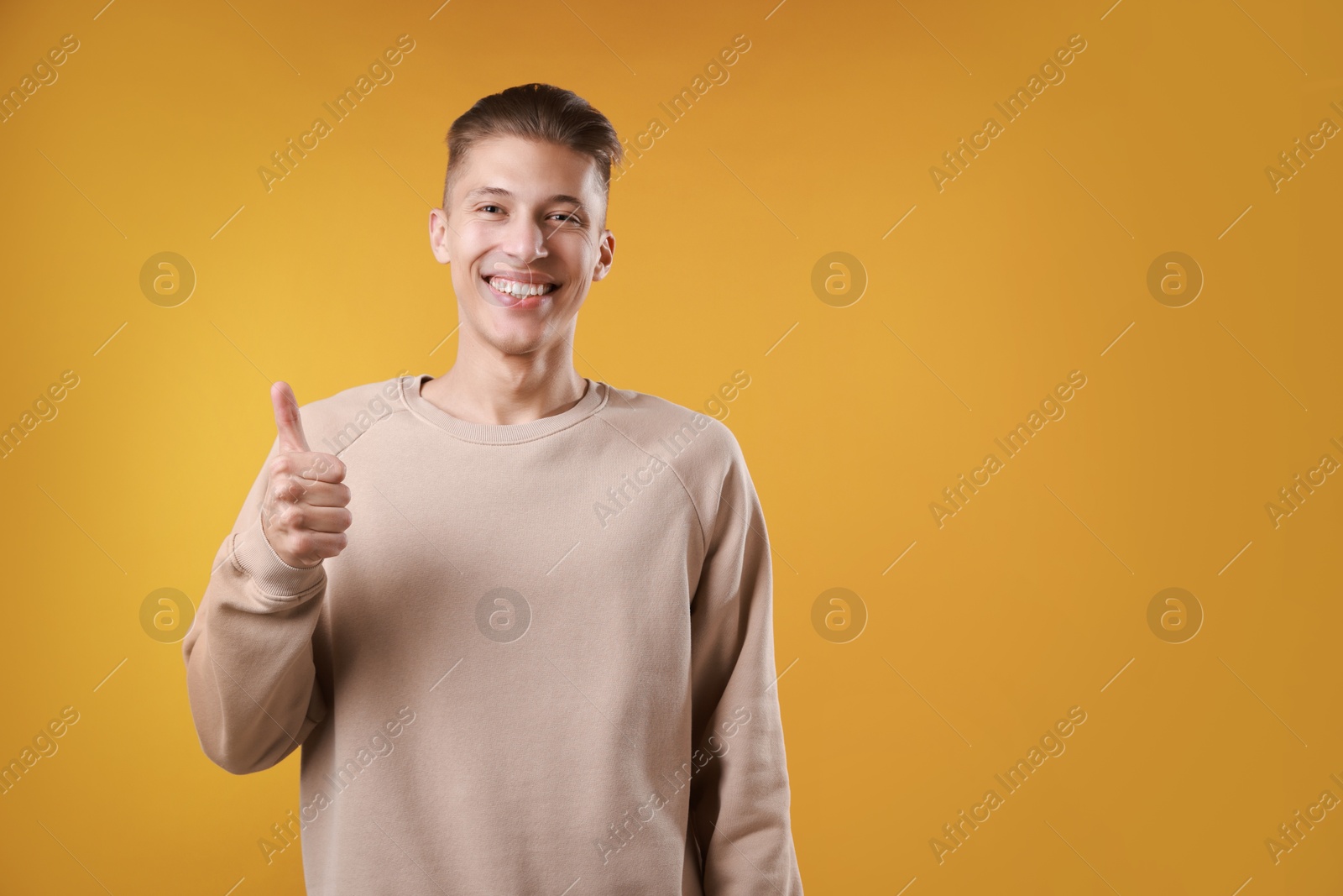 Photo of Happy man showing thumbs up on orange background, space for text. Like gesture