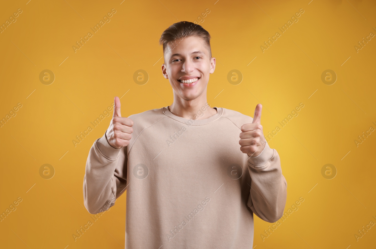 Photo of Happy man showing thumbs up on orange background, space for text. Like gesture