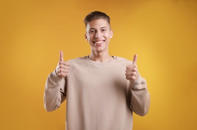 Photo of Happy man showing thumbs up on orange background, space for text. Like gesture