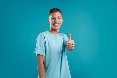 Photo of Happy man showing thumbs up on light blue background. Like gesture