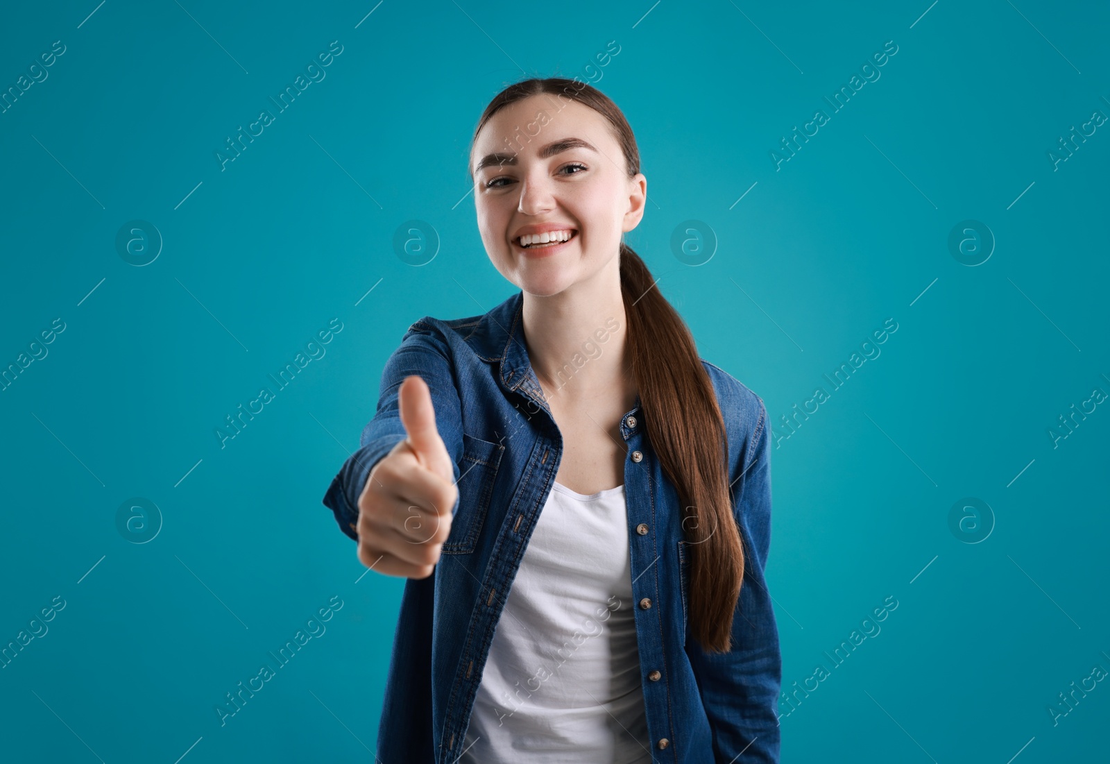 Photo of Happy woman showing thumbs up on light blue background. Like gesture