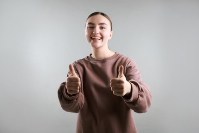 Photo of Happy woman showing thumbs up on grey background. Like gesture