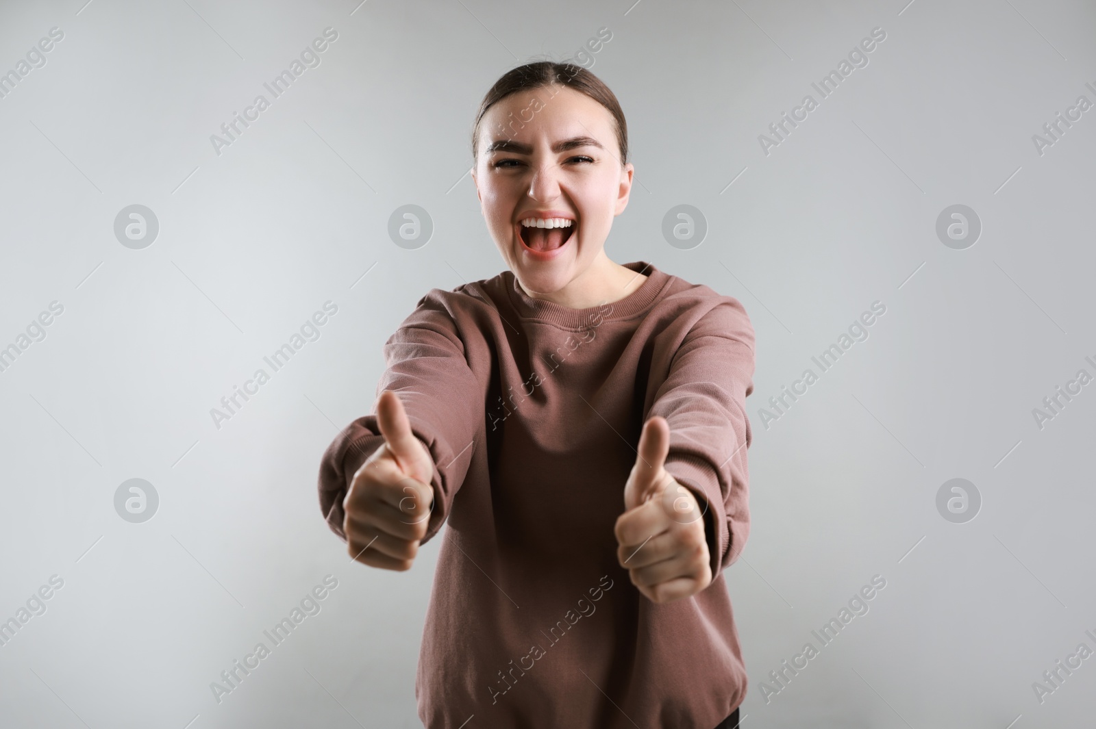 Photo of Emotional woman showing thumbs up on grey background. Like gesture