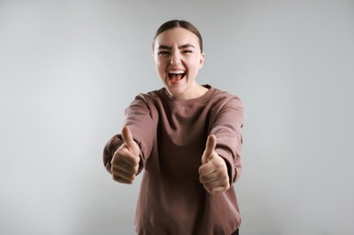 Photo of Emotional woman showing thumbs up on grey background. Like gesture