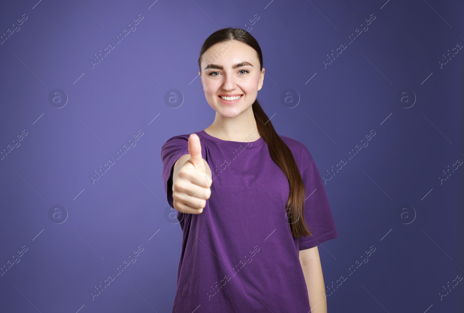 Photo of Happy woman showing thumbs up on purple background. Like gesture