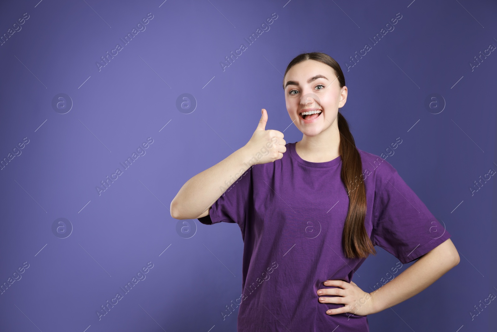 Photo of Happy woman showing thumbs up on purple background, space for text. Like gesture