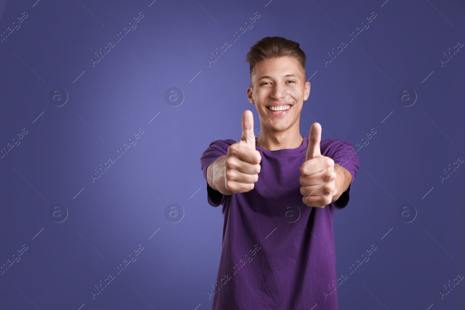 Photo of Happy man showing thumbs up on purple background, space for text. Like gesture