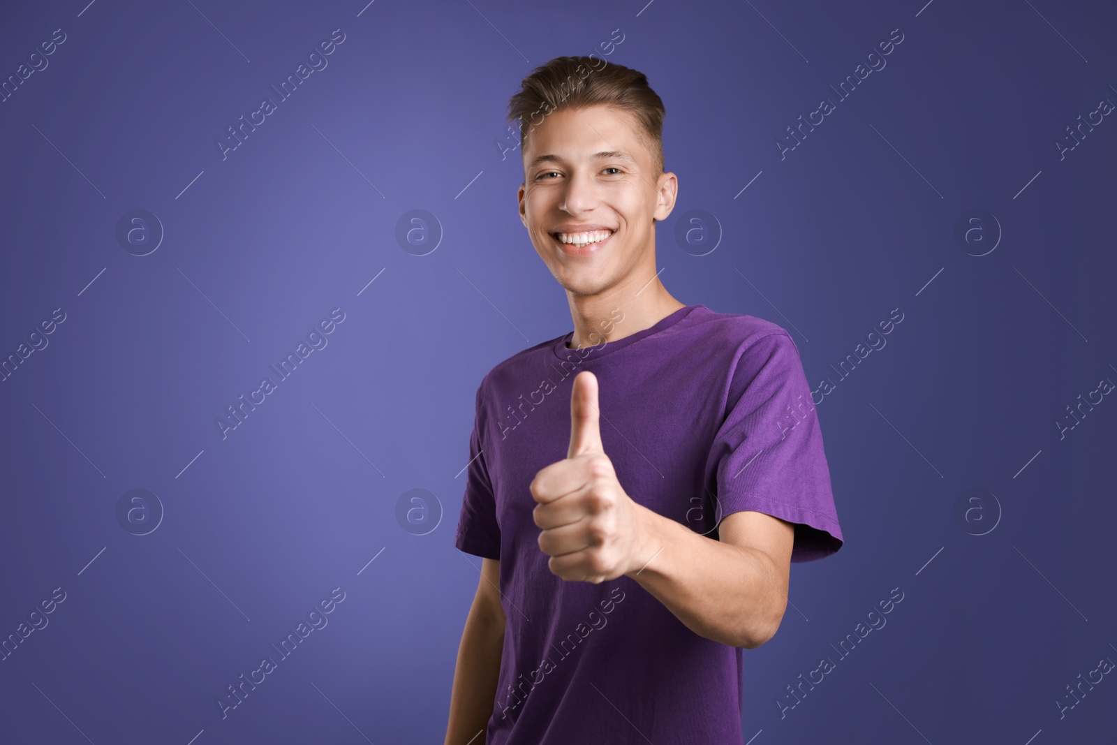 Photo of Happy man showing thumbs up on purple background, space for text. Like gesture