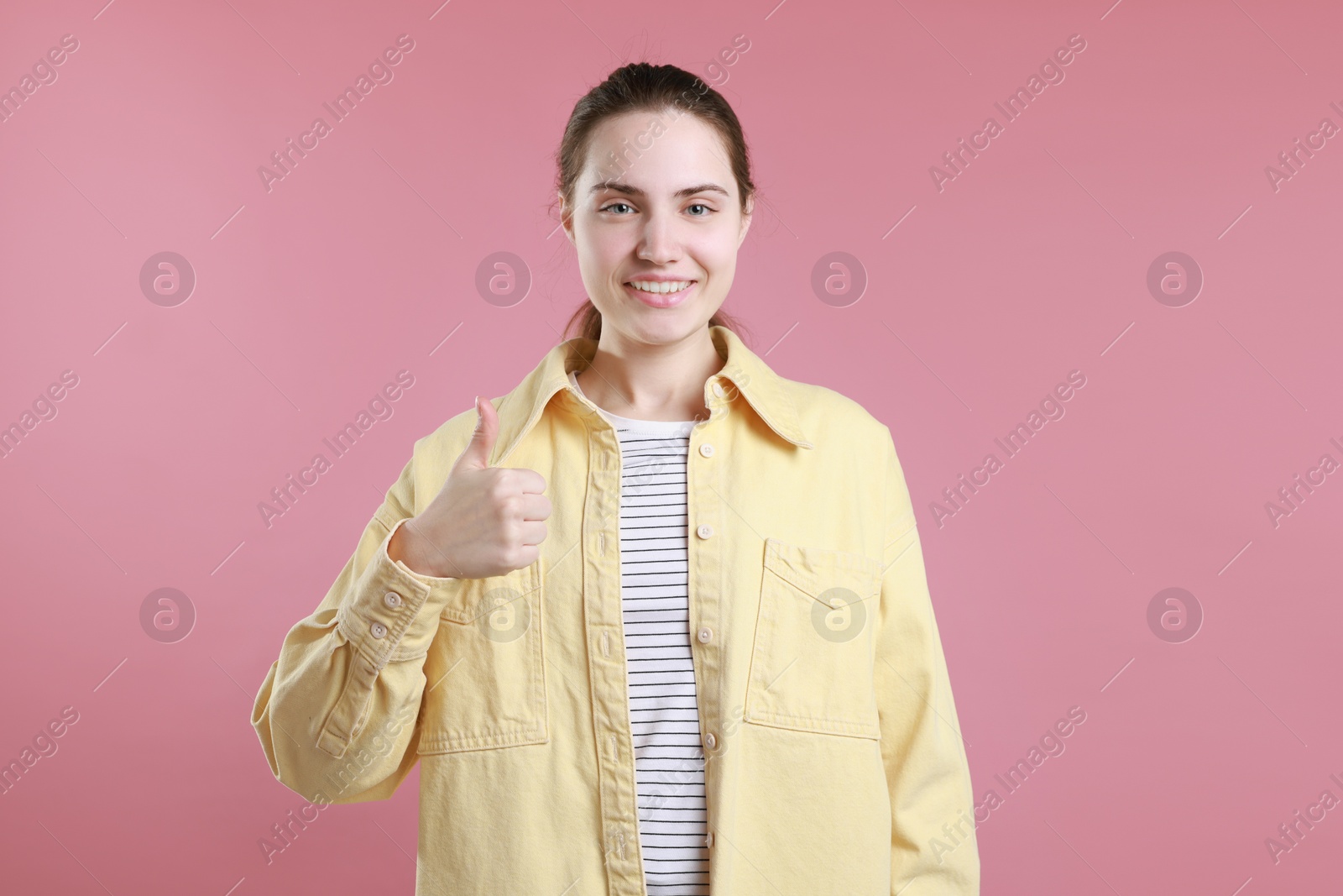 Photo of Happy woman showing thumbs up on pink background. Like gesture