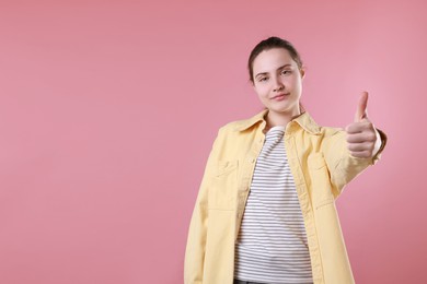 Woman showing thumbs up on pink background, space for text. Like gesture