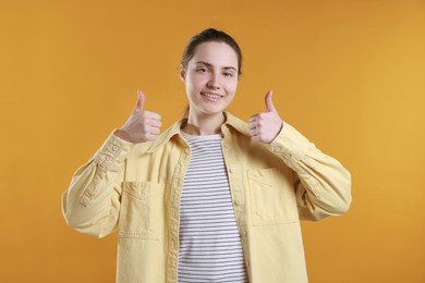 Photo of Happy woman showing thumbs up on orange background. Like gesture