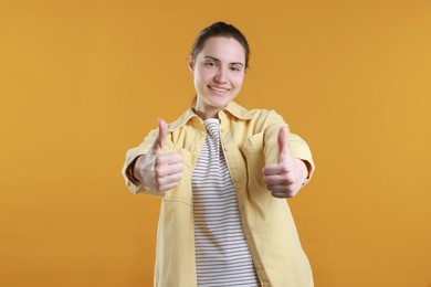 Photo of Happy woman showing thumbs up on orange background. Like gesture