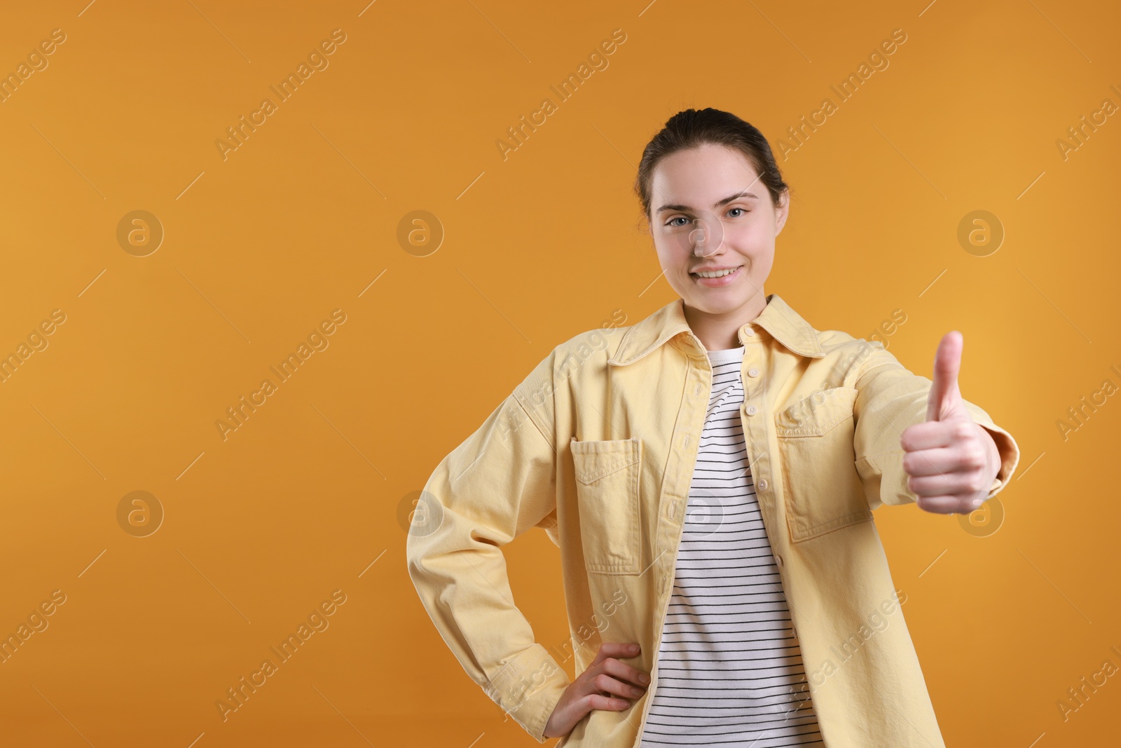 Photo of Happy woman showing thumbs up on orange background, space for text. Like gesture