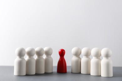 Photo of Human resources concept. Red figure among wooden ones on table against light background, closeup. Space for text