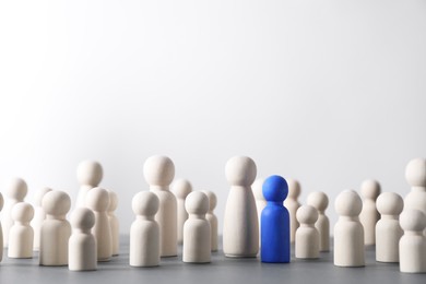 Photo of Human resources concept. Blue figure among wooden ones on table against light background, closeup. Space for text