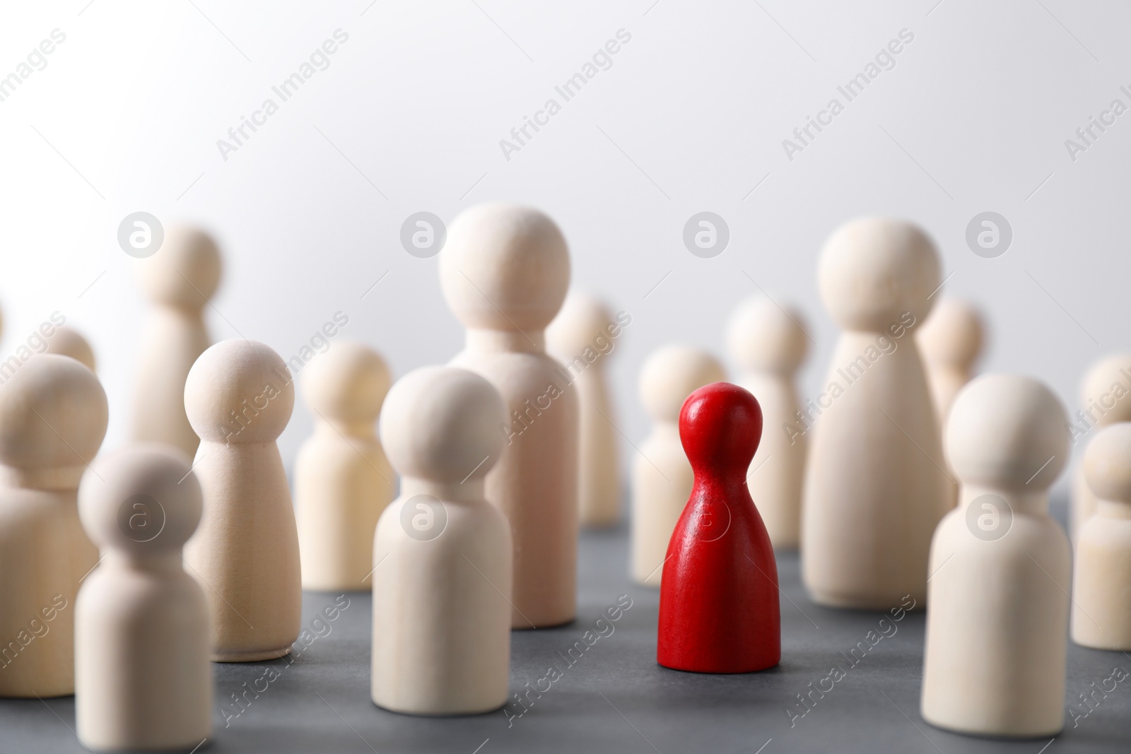 Photo of Human resources concept. Red figure among wooden ones on table against light background, closeup