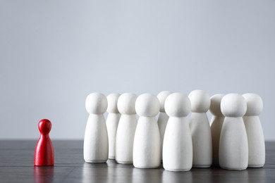 Photo of Human resources concept. Red figure in front of wooden ones on table against light background, closeup. Space for text