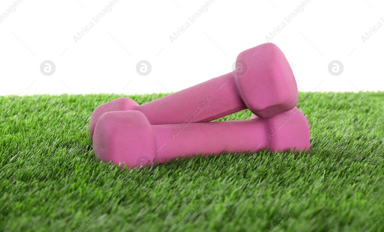 Photo of Dumbbells on artificial grass isolated on white. Sport equipment