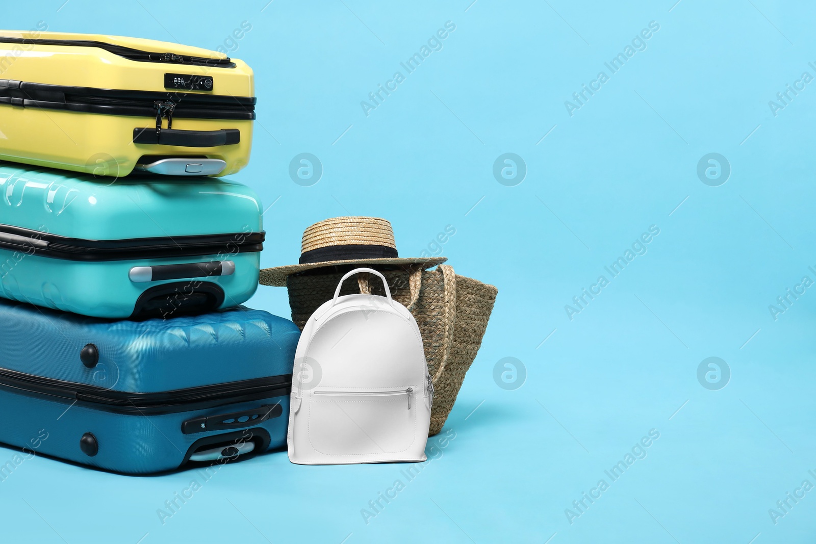 Photo of Colorful suitcases, backpack, beach bag and straw hat on light blue background. Space for text