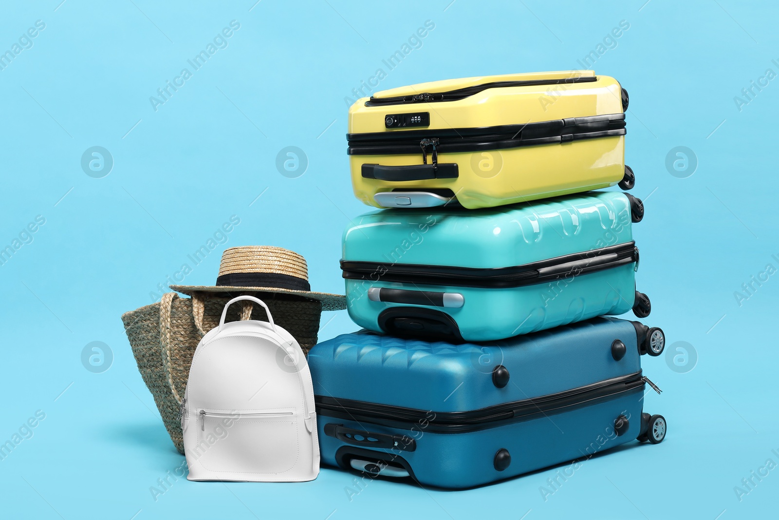 Photo of Colorful suitcases, backpack, beach bag and straw hat on light blue background